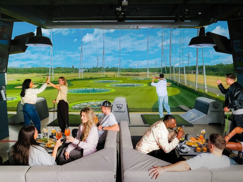Junge Menschen in einem Golfclub bei der driving range Foto: Topgolf Wien